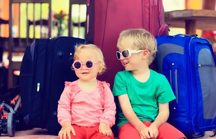 little boy and toddler girl sitting on suitcases ready to travel, kids travel concept