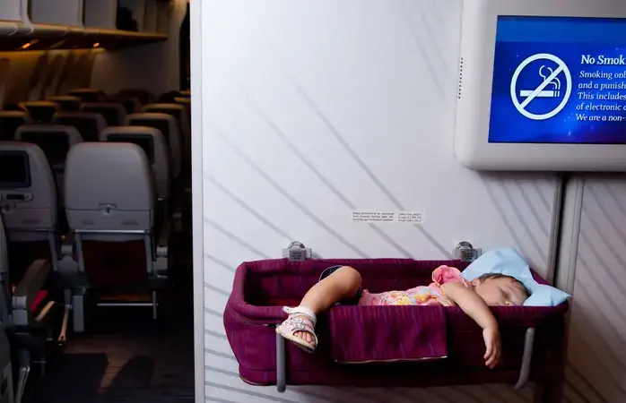 Travel with children. Small two year old baby girl sleep in a special bassinet on a airplane