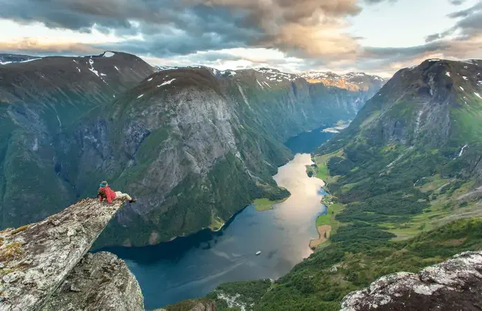 Man sits on the edge of an overhanging rock to admire the view over Naeroyfjord near Gudvangen in Norway