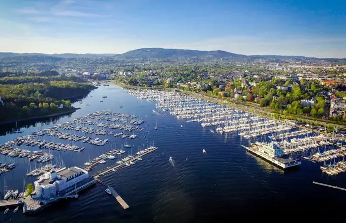 Frognerkilen bay photographed from the air with a drone. Yachts and leisure boats are parked at the marina. The forested area to the left, near the waterside, is Bygdøy. The European route E18 runs along the shore. In th background are the far away mountains that can be seen on the horizon and the clear blue sky of a day in May.
Frognerkilen is a bay in the inner Oslofjord of Norway, east of the Bygdøy peninsula.
It was an important shipping port for timber in the 17th and 18th centuries, but today a large part of the bay is used as a harbour for leisure boats.